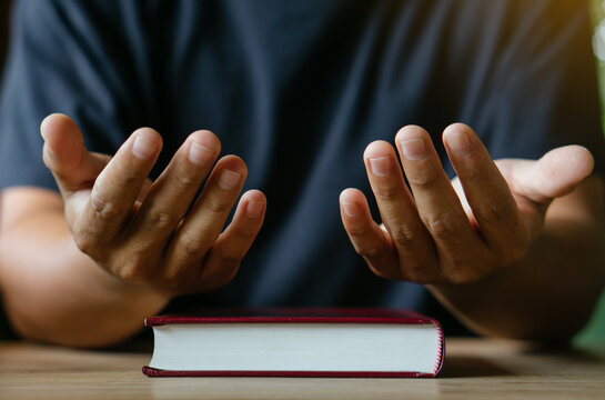 Hands of man with Bible praying.Christian life prayer to god. Man Pray for god.believe in goodness. Holding hands in prayer on a wooden table.