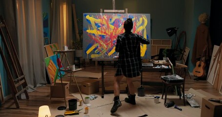 Angry painter spends evening in artist's studio in hand she holds container of red paint and brush she walks up to canvas with strong quick motion splashes color on painting, she throws out emotions