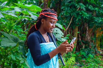 A happy female african with local beads on her head and farming hoe on her shoulder, looks into the...