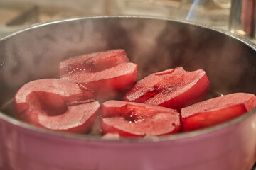 Cut pears are boiled in red syrup with wine on gas stove