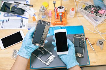 Phone repair concept a male phone repairman wearing gloves and a mask checking the components of...
