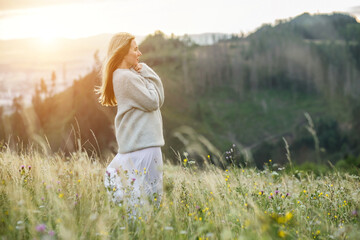 Fototapeta na wymiar Happy woman enjoying sunset stay on the green grass on the forest peak of mountain. Fresh air, Travel, Summer, Fall, Holidays, Journey, Trip, Lifestyle. 