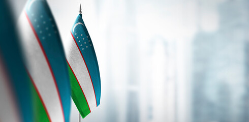 Small flags of Uzbekistan on a blurry background of the city - obrazy, fototapety, plakaty