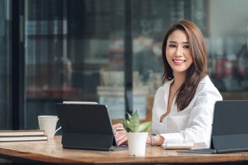 Portrait of young beautiful asian woman smiling and looking at camera while sitting at her office...