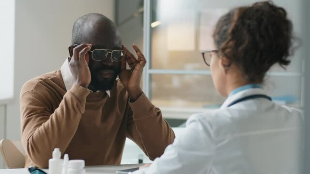 Over the shoulder shot of African American man complaining about headache to female doctor during medical consultation in clinic