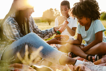 Black happy family eating hotdogs during picnic on field