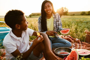 Black family eating watermelon during picnic on summer field