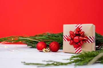 Christmas gift in craft paper on a background of coniferous branches and shiny balls.
