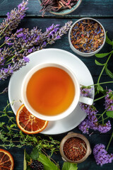 A cup of tea with dry fruit, flowers, and herbs, shot from above on a dark rustic wooden background