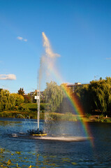 Fototapeta premium Close-up view of fountain with a beautiful rainbow. Blue sky background. A rainbow made in water fountain. Scenic autumn landscape