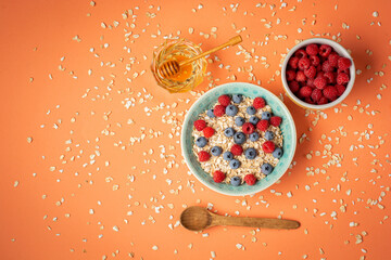 Healthy breakfast - oatmeal with honey, blueberries and raspberries on orange background. Flat lay