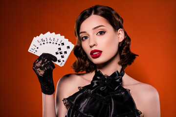 Photo of charming rich stunning young woman hold hands cards play poker dealer isolated on dark orange color background - obrazy, fototapety, plakaty