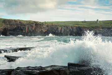 Powerful waves crushing against Cliffs and rough stone coastline of West coast of Ireland. Doolin area. County Clare. Ocean power and rugged Irish coastline. Green fields in the background