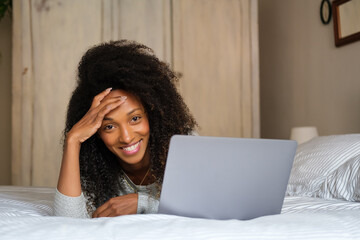 Cheerful afro hairstyle woman lying on her bed for watching online content on her laptop.. Home leisure and relax concept.