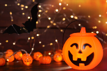 Fototapeta premium Glowing Halloween handbag in the form of a pumpkin, bat on wooden background with bokeh lights.Halloween trick or treat!Сopy space for text.Halloween background