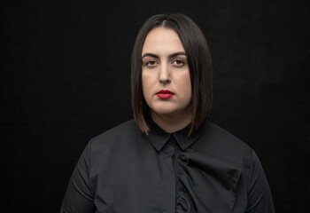 Studio portrait of a plump, round-faced woman 30-35 years old with black hair on a black background, with brightly painted red lips, dark tone. Perhaps she is a director or a television announcer, 