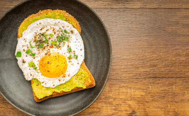 Toast with avocado and eggs served on a plate on a wooden table. Top view. Space for text. Healthy fruit concept