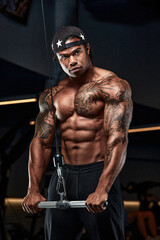 Obraz na płótnie Canvas Strong and muscular afro-american man trains on modern equipment in gym. Portrait of muscular pumped up fitness trainer