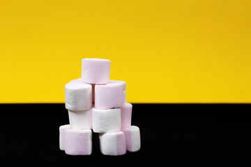 Tower of marshmallow candies on a yellow and black background. Close-up