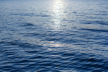 Naklejka premium Blue sea waves surface, ripple water texture, beautiful quiet ocean background, abstract aqua pattern backdrop, sunset reflection, sun light glow, dark night shiny moonlight at lake, river, top view