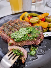 Veal steak on a black plate with spices and vegetables.