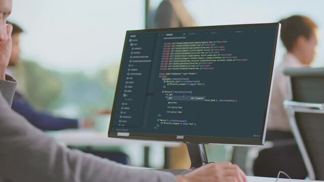 Coding in software company. Developing new application, writing code on dark background. Modern open space office interior.