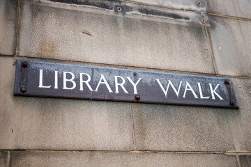 Library Walk sign on old stone wall.  Metal sign with white text.