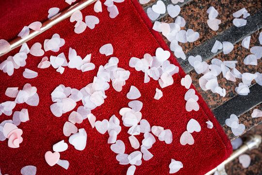 Beautiful Wedding Confetti Love Heart Shape Scatter On Red Carpet After Being Thrown Over Bride And Groom To Celebrate Marriage Ceremony. Romantic Love Hearts On The Ground.