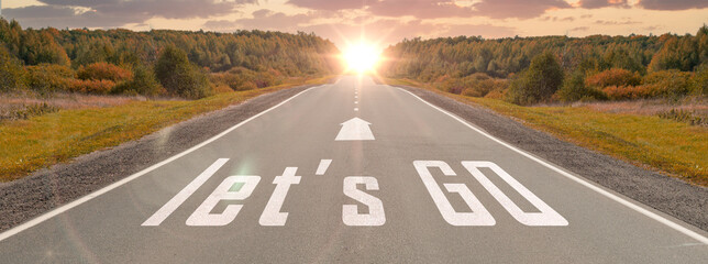 word let's go written on highway road in the middle of empty asphalt road at beautiful sunset sky....