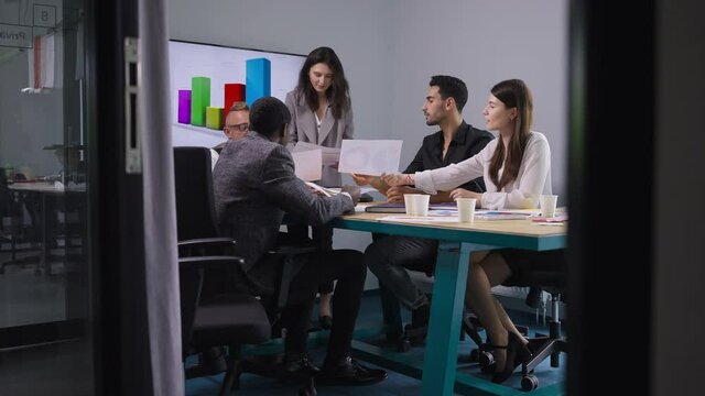 Wide shot group of colleagues brainstorming in meeting room in office indoors. Positive confident professional men and women talking analyzing paperwork planning strategy idea