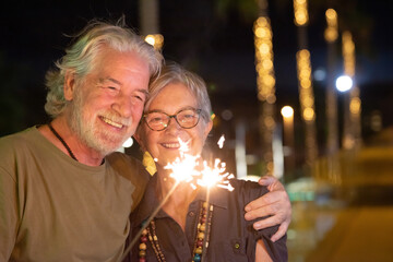 Beautiful old senior couple in outdoor at night having fun with sparkles lights. Two smiling...