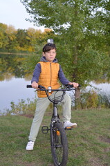 Fototapeta na wymiar A boy in an orange jacket is sitting on a bicycle. There is an action camera on his head.