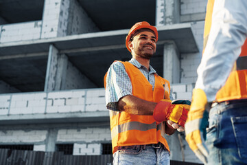 Two men engineers in workwear shaking hands against construction site.