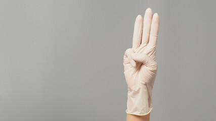 A hand sign of 3 fingers point upward meaning protest or three on grey background.Hand wear medical glove.