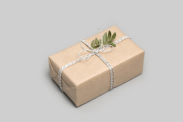 Small gift box wrapped in craft paper with dried boxwood leaves on solid gray background. Modern minimal present suitable for any occasion. Neutral holiday backdrop with copy space. Isometric view