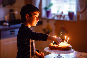 Adorable happy blond little kid boy celebrating his birthday. Child blowing candles on homemade baked cake, indoor. Birthday party for school children, family celebration, fireworks