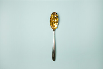 Metal spoon of Omega-3 capsules on blue background with copyspace