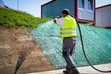 Worker planting grass with pipe. Green liquid mixture with seeds, humus and other ingridients for...