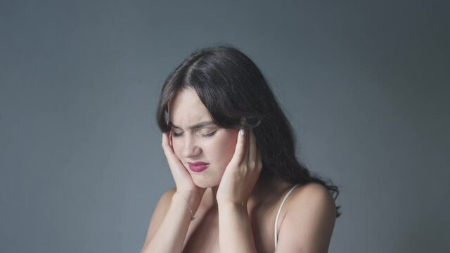 beautiful young woman eyes closed covering ears with hands and shaking head suffering from loud noise or headache. pretty female brunette fringe showing negative gesture don't want to listen hear. 