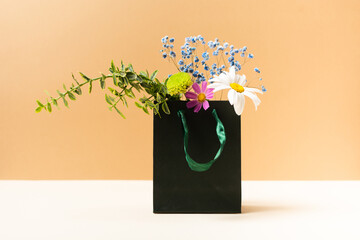 Paper bag with beautiful summer garden flowers and plants on beige background