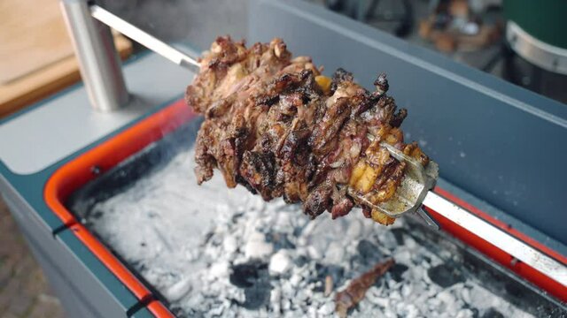 Top view of professional bq smoker with burning charcoal and ash, juicy pork meat pieces slowly rotating on metal skewer and juicy fat dropping inside the smoker. Traditional grilled pork preparation