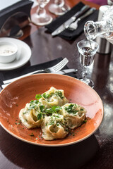 Manti dumplings with minced lamb meat on orange plate and vodka on the table