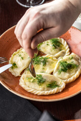 Polish Pierogi or Vareniki dumplings stuffed with potato served with dill on orange plate
