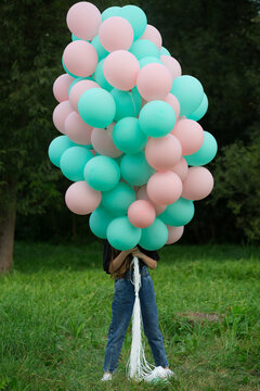 A girl in nature covered her face with pink and tiffany balloons