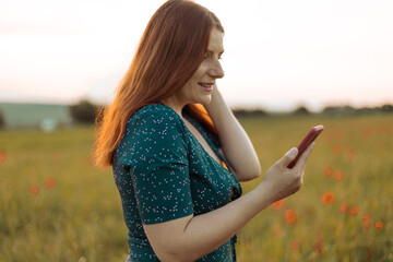 Caucasian Happy beautiful young woman using mobile phone outdoors in a summer field at sunset. Tourism, traveling and healthy lifestyle concept.