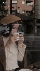 Young woman drinking a hot cup of coffee in cafeteria. Parisian Vibes Style for Autumn Season 2021.