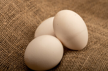 White chicken eggs on homespun fabric with a rough texture, close-up selective focus.