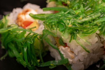 Delicious sushi roll with Philadelphia cheese, cucumber, salmon and chuka in a plastic tray on a wooden table.