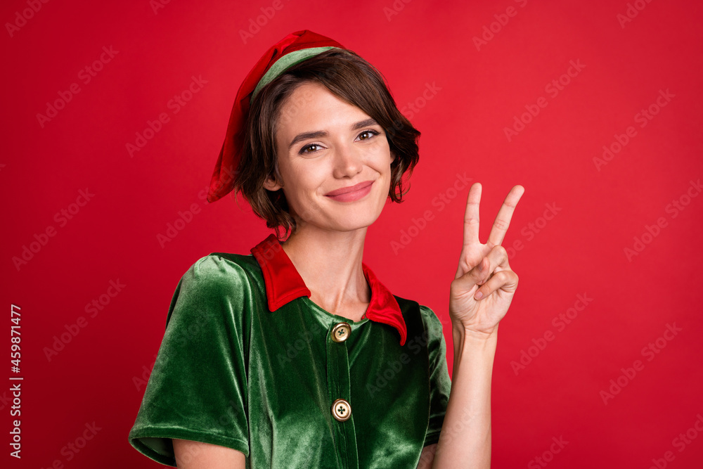 Wall mural Photo of friendly helper assistant pretty lady show v-sign wear elf costume hat isolated red color background