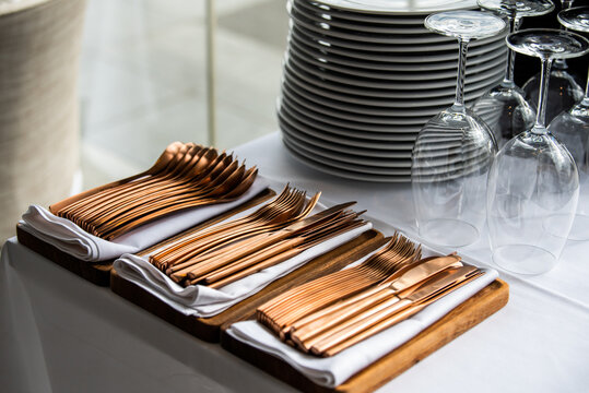 Copper, or rose gold, silverware set in a box, with glasses and main dishes in a restaurant before service. cutlery
